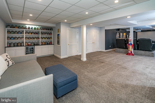carpeted living area featuring baseboards, a dry bar, a drop ceiling, and beverage cooler