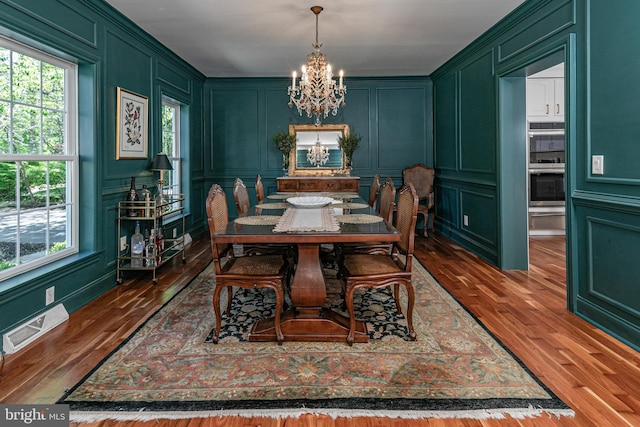 dining space with visible vents, a decorative wall, a notable chandelier, and wood finished floors