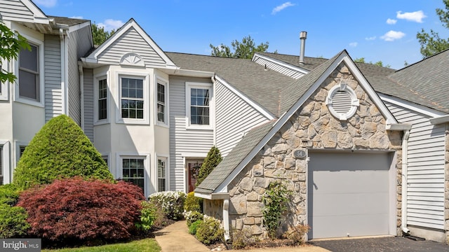 view of front of home with aphalt driveway, a garage, a shingled roof, and stone siding