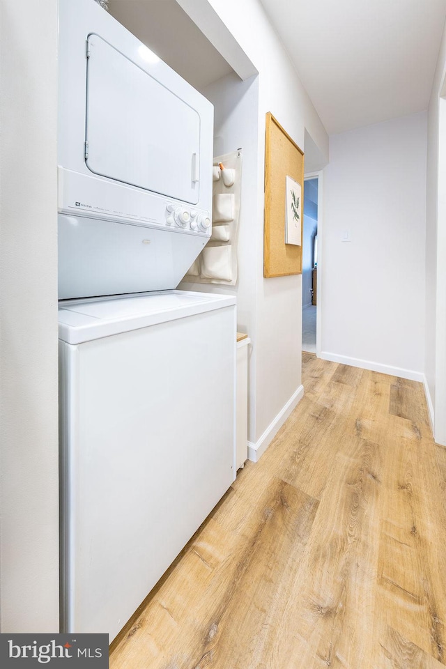 washroom featuring stacked washer / drying machine, light wood-style floors, and baseboards