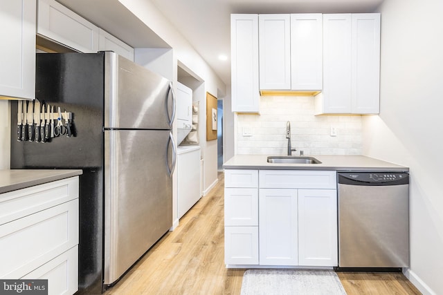 kitchen featuring a sink, stainless steel appliances, stacked washing machine and dryer, light wood-style flooring, and tasteful backsplash
