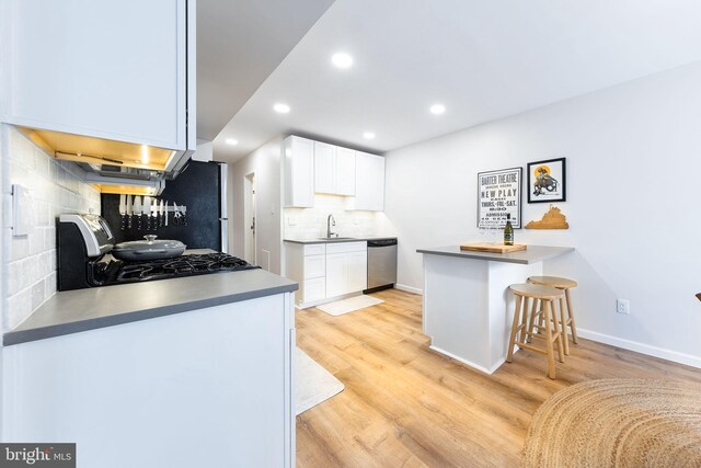 kitchen featuring dishwasher, range, a peninsula, a sink, and white cabinets