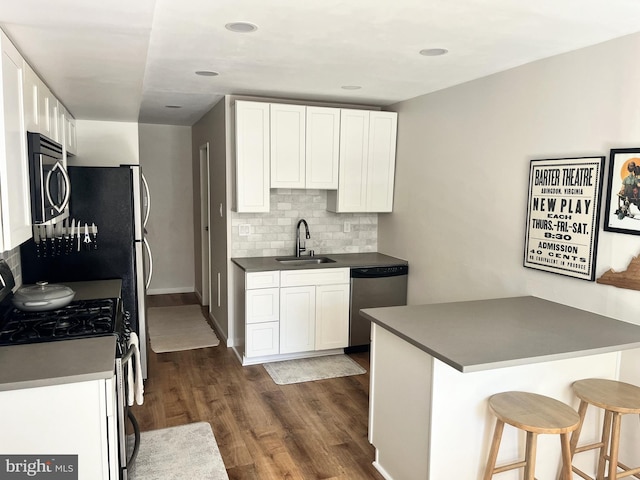 kitchen with appliances with stainless steel finishes, a sink, decorative backsplash, dark wood-type flooring, and dark countertops