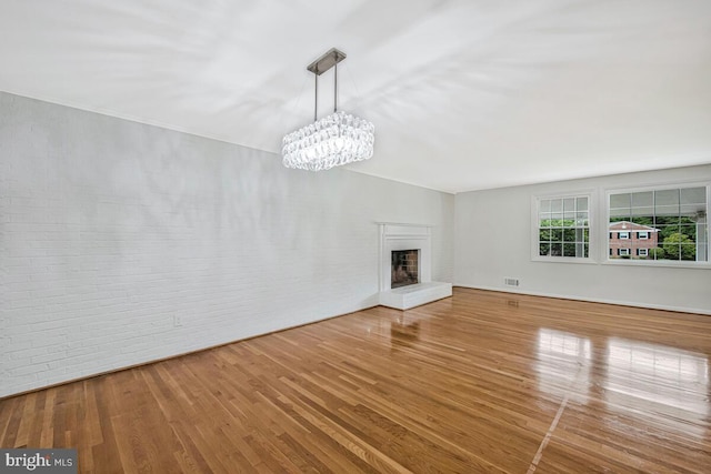 205 Dunbeath Ct, Lutherville Timonium, MD 21093 - unfurnished living room featuring wood finished floors, a chandelier, a fireplace with raised hearth, and brick wall