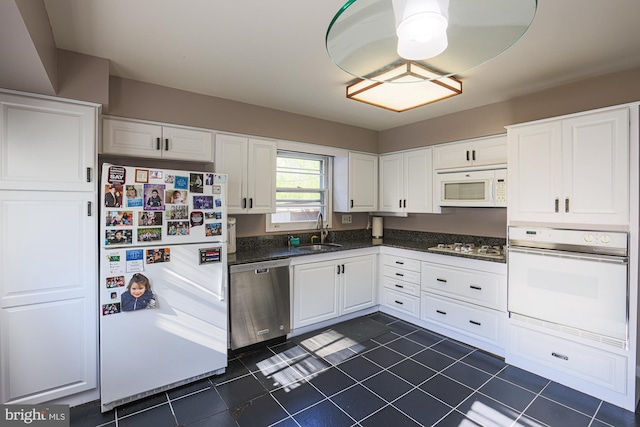 kitchen featuring dark tile patterned floors, a sink, white cabinetry, and white appliances