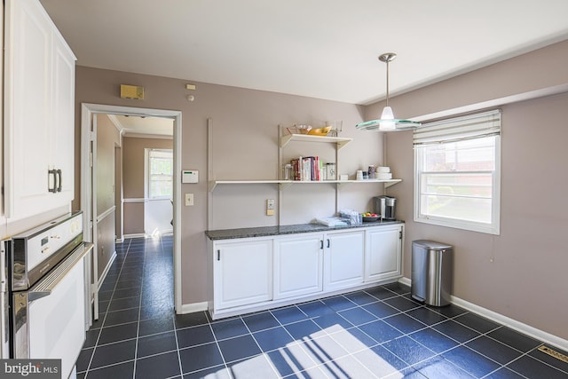 kitchen with baseboards, white oven, dark tile patterned floors, white cabinetry, and dark stone countertops