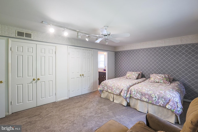 bedroom featuring ceiling fan, visible vents, track lighting, two closets, and carpet