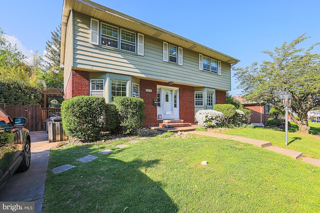 colonial home featuring brick siding, a front lawn, fence, and entry steps