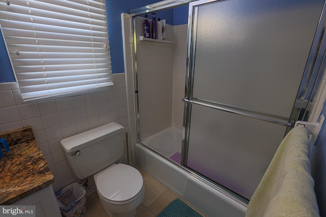 bathroom featuring vanity, toilet, tile walls, tile patterned floors, and combined bath / shower with glass door
