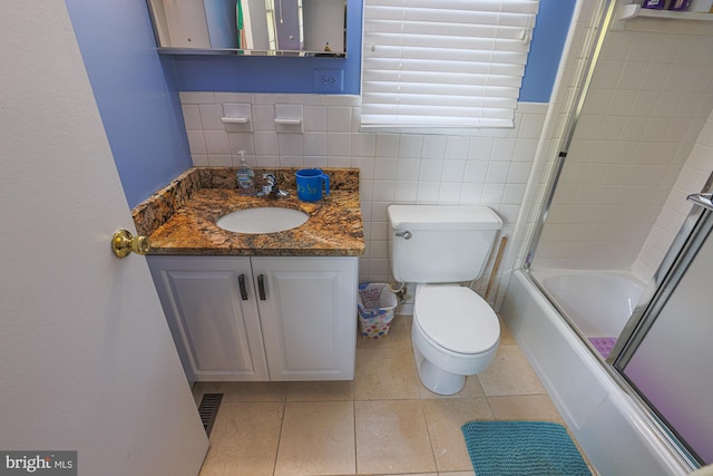 bathroom with vanity, tile patterned flooring, toilet, tile walls, and bath / shower combo with glass door