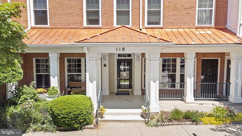 view of exterior entry featuring brick siding, covered porch, and a standing seam roof