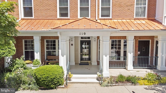 view of exterior entry featuring brick siding, covered porch, and a standing seam roof