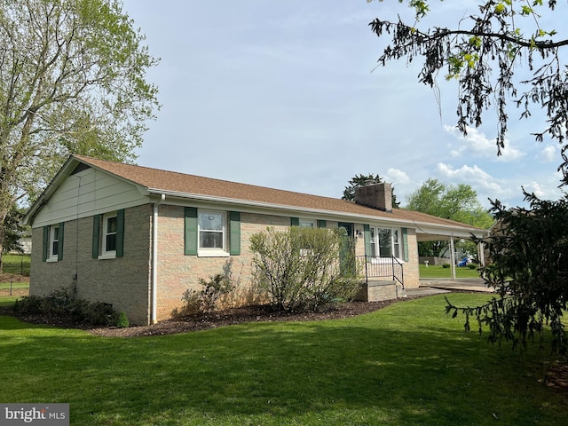 rear view of house with a carport, a chimney, a yard, and brick siding
