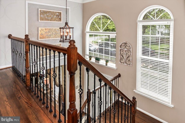 stairs with baseboards, crown molding, wood finished floors, and a notable chandelier