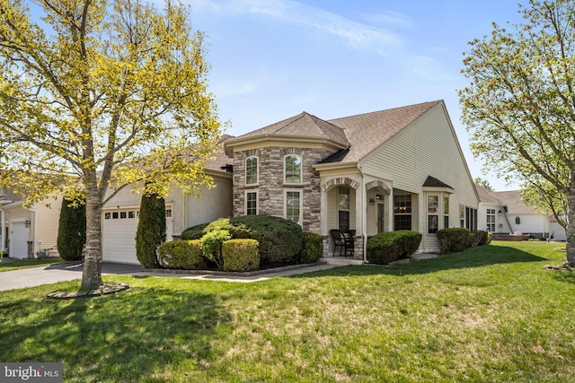 french country inspired facade featuring roof with shingles, an attached garage, a front lawn, aphalt driveway, and stone siding