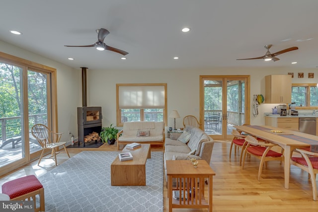 living room featuring light wood-style floors, a wood stove, a ceiling fan, and recessed lighting