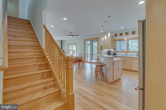 kitchen with light wood-style floors, a kitchen breakfast bar, ceiling fan, light countertops, and a sink