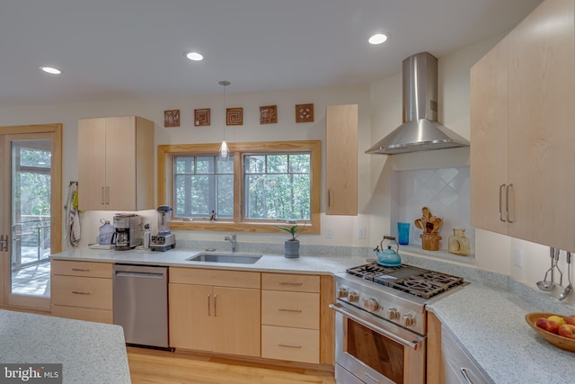 kitchen with wall chimney range hood, hanging light fixtures, a sink, light brown cabinets, and stainless steel appliances
