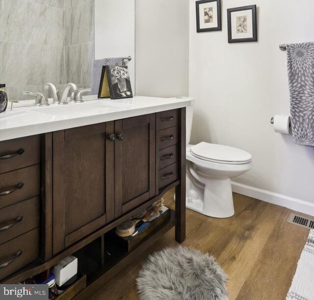 bathroom featuring vanity, toilet, baseboards, wood finished floors, and visible vents