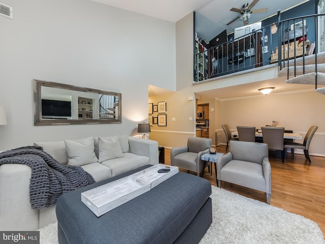 living area with ceiling fan, visible vents, a towering ceiling, wood finished floors, and baseboards