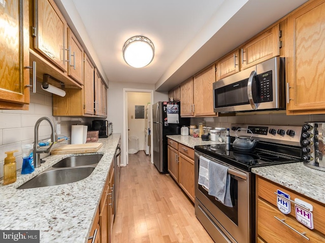 kitchen featuring decorative backsplash, brown cabinetry, a sink, light wood finished floors, and stainless steel appliances