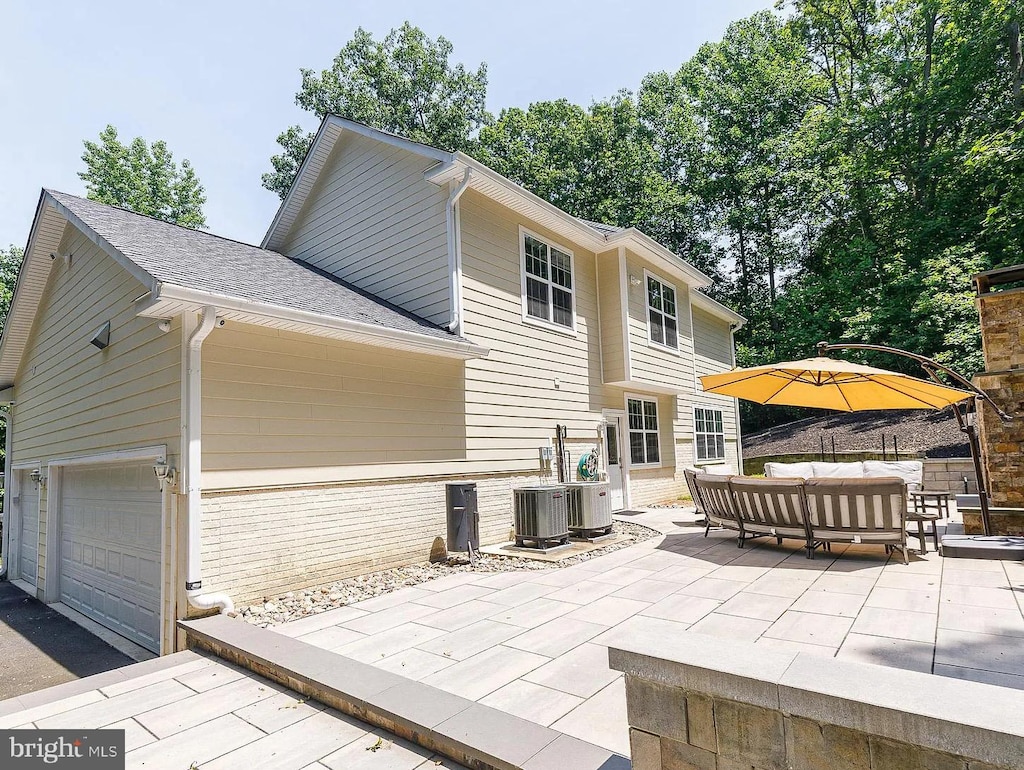 rear view of property with a garage, central air condition unit, brick siding, a patio, and outdoor lounge area