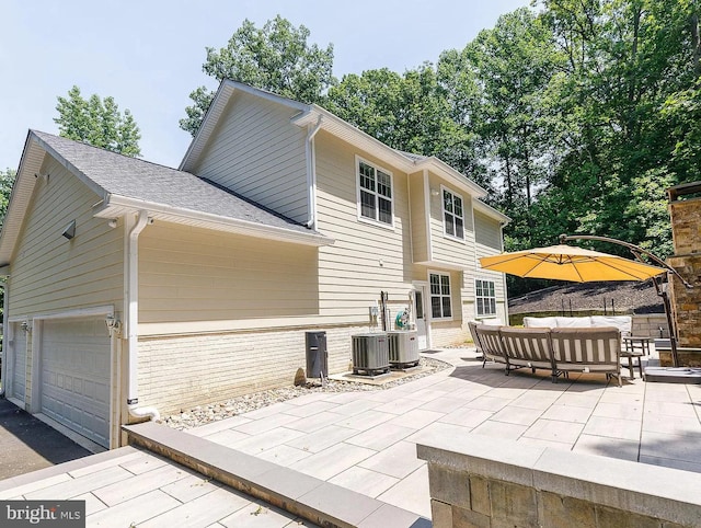 rear view of property with a garage, central air condition unit, brick siding, a patio, and outdoor lounge area