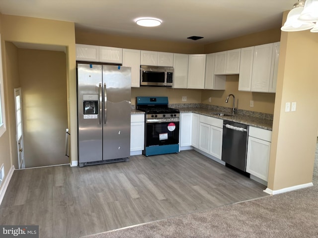 9016 Samoset Rd, Randallstown, MD 21133 - kitchen featuring stone countertops, white cabinets, a sink, light wood finished floors, and appliances with stainless steel finishes