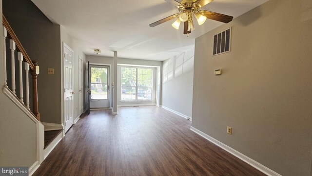 interior space with dark wood-style flooring, a ceiling fan, baseboards, visible vents, and stairway