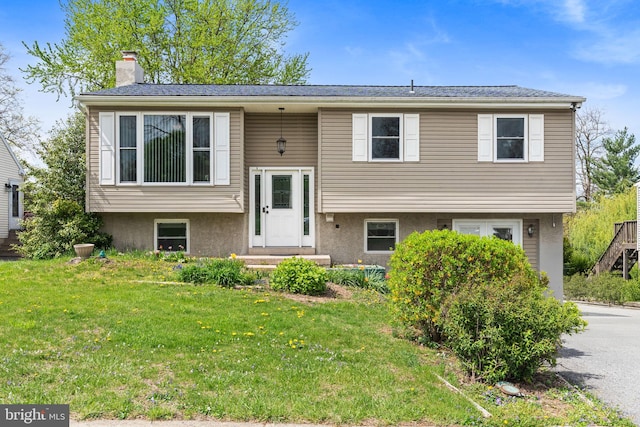 bi-level home featuring stucco siding, a front yard, and a chimney