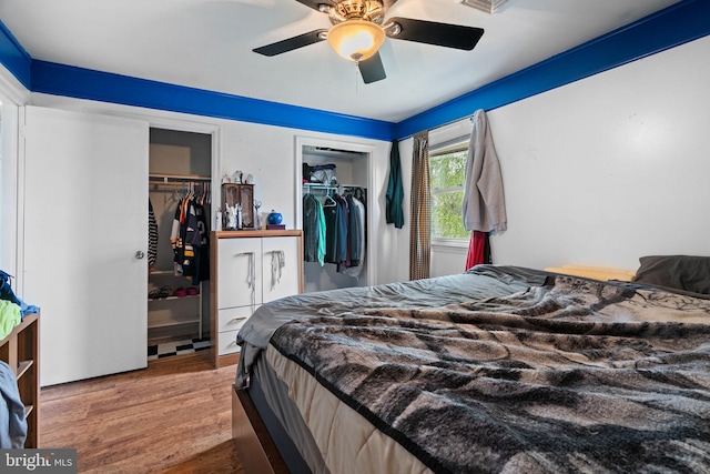 bedroom with a ceiling fan, two closets, and wood finished floors