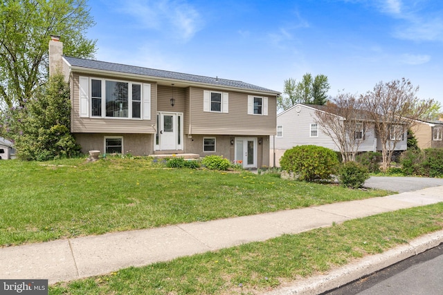 bi-level home featuring a chimney and a front lawn