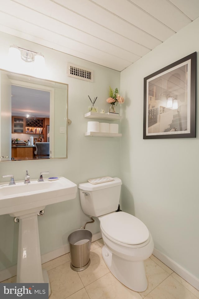 half bath with baseboards, tile patterned flooring, toilet, and visible vents