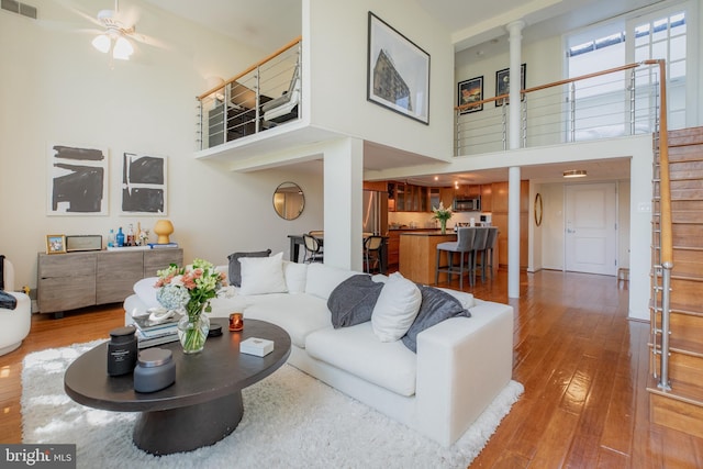 living room featuring a ceiling fan, decorative columns, visible vents, a high ceiling, and hardwood / wood-style floors
