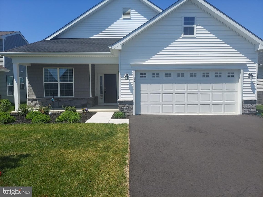 view of front of home featuring an attached garage, aphalt driveway, covered porch, and a front yard
