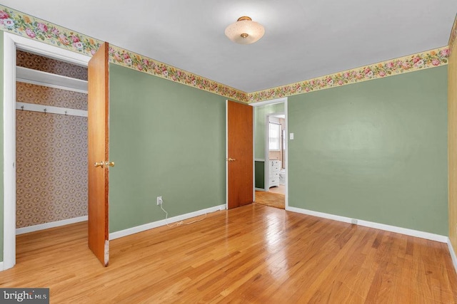unfurnished bedroom with baseboards, wallpapered walls, and wood finished floors