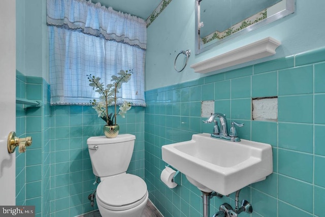 half bath with a sink, tile walls, and toilet