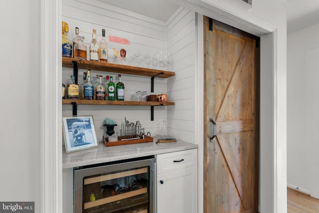 bar with wine cooler, indoor wet bar, light wood-type flooring, and a barn door