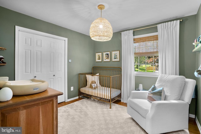 bedroom featuring a crib, baseboards, light wood finished floors, and a chandelier