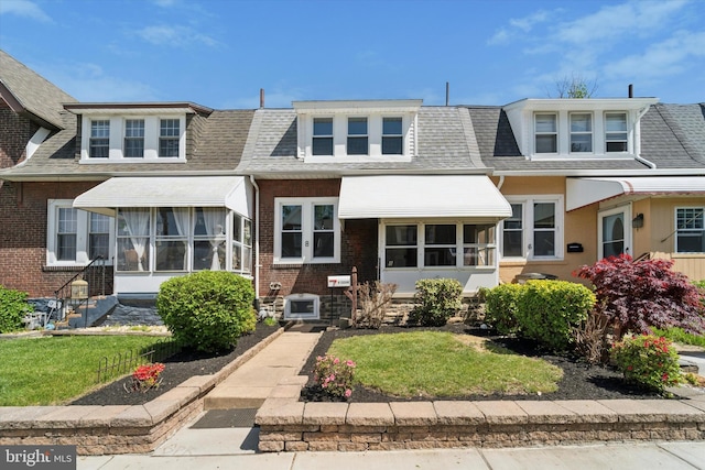 view of front of home with brick siding, a shingled roof, and a front lawn