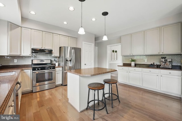 kitchen featuring under cabinet range hood, stainless steel appliances, decorative backsplash, and light wood-style floors