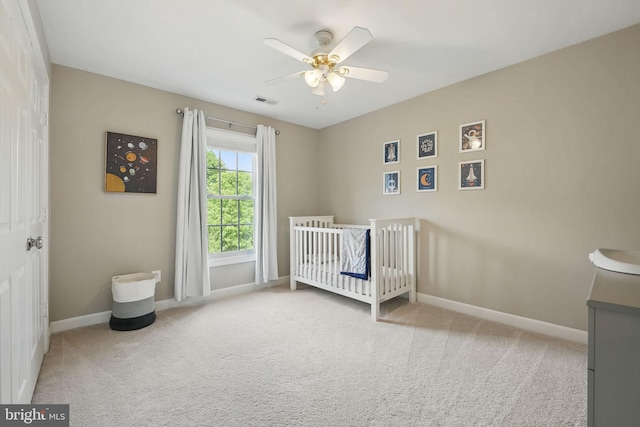 bedroom with visible vents, baseboards, a crib, a ceiling fan, and carpet