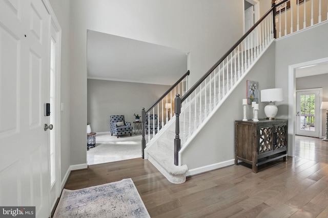 entrance foyer with stairs, baseboards, wood finished floors, and a high ceiling