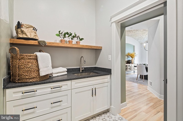 bar featuring vaulted ceiling, a sink, baseboards, a chandelier, and light wood-style floors