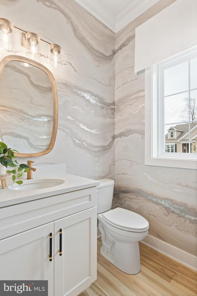 half bathroom featuring toilet, ornamental molding, wood finished floors, and vanity