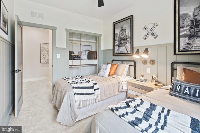 bedroom featuring ceiling fan, visible vents, a wainscoted wall, carpet, and a decorative wall