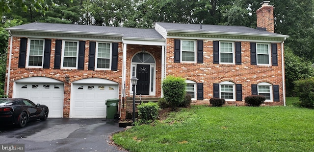 split foyer home with a garage, a front yard, a chimney, brick siding, and driveway