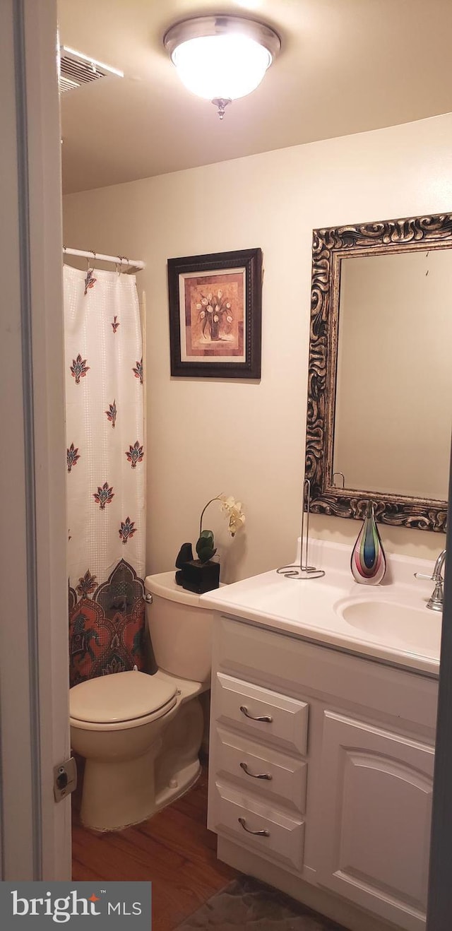 bathroom with vanity, toilet, wood finished floors, a shower with curtain, and visible vents