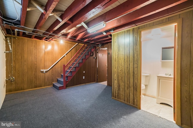 basement featuring wood walls, a sink, baseboards, stairway, and carpet flooring