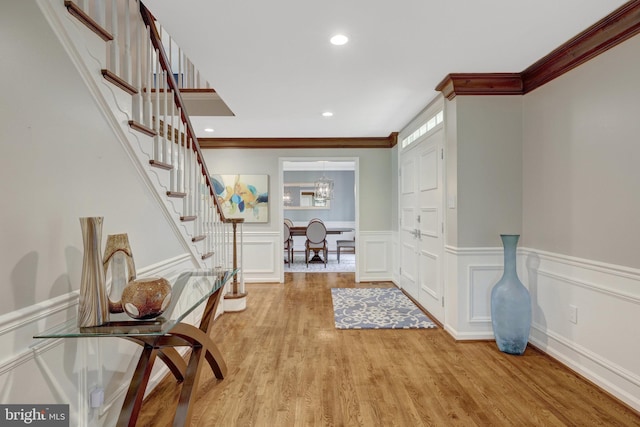 entrance foyer with light wood-style flooring, a wainscoted wall, crown molding, stairway, and a decorative wall